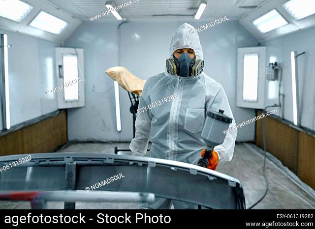 Car painter wearing protective clothes, mask painting automobile part using sprayer
