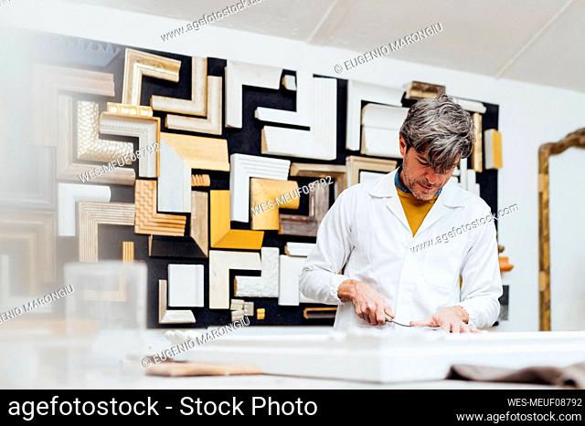 Craftsman preparing picture frame at workbench in workshop