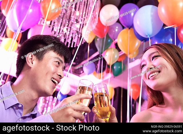 Two friends celebrating, toasting with champagne, nightclub in Beijing, balloons in the background
