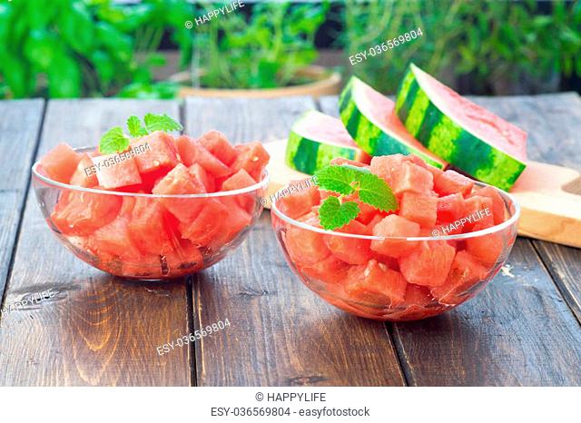 Watermelon cut in small cubes and served in two glas dishes on wooden table in rustic style
