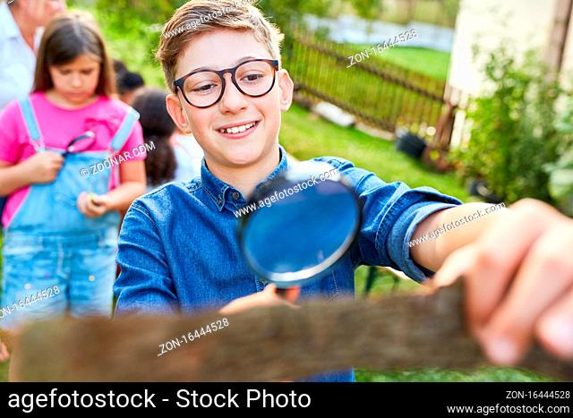 Junge untersucht neugierig ein Stück Baumrinde mit Lupe im ökologischen Sommercamp