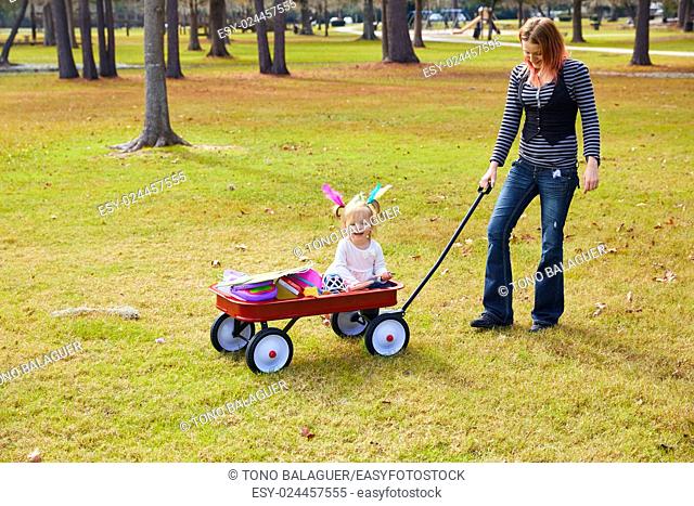 Kid girl and mother walking in the park with pull cart
