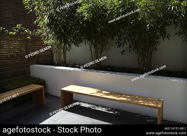 Compact, contemporary town garden/patio in the Islington area of North London, UK, designed by Modular. With retaining wall containing raised bed planted with...