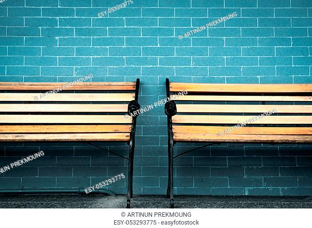 Empty two wooden bench on green brick wall background. Waiting for someone to full fill empty wooden chair. Brown wooden bench outside the building