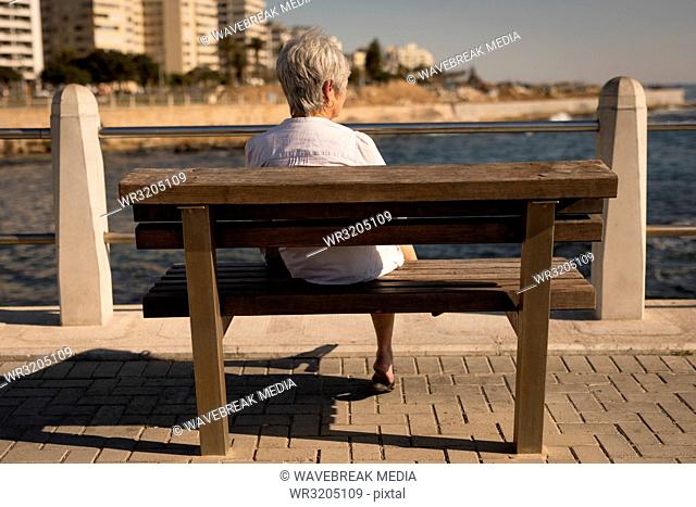 Senior woman sitting on bench sea side at promenade