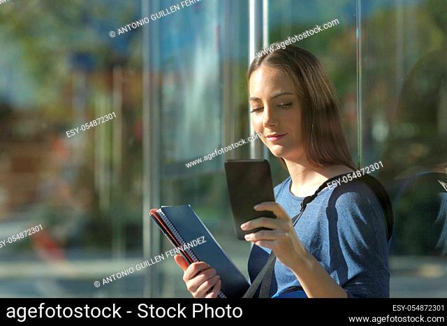 Student checking smart phone at the bus station monitoring transport through the app