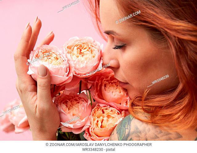 Red-haired cute woman is sniffing a bouquet of pink Buttercup Asian on a pink background. Mother's Day