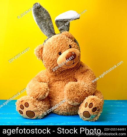 big cute brown teddy bear wearing a rabbit mask with long ears on his head, funny holiday Easter card