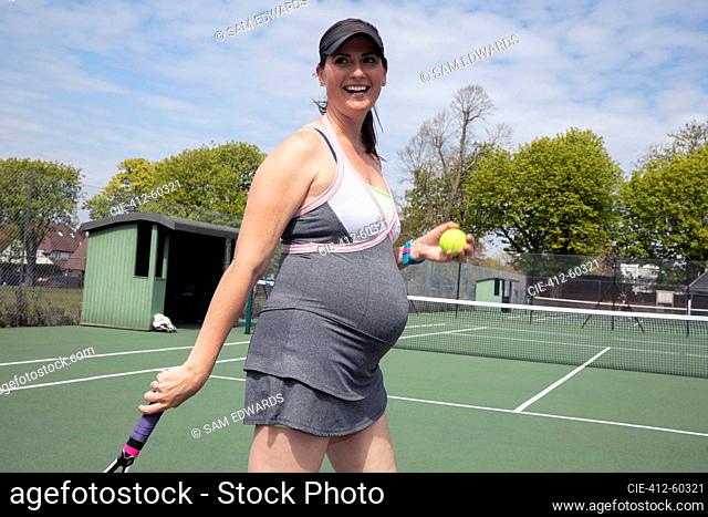 Happy pregnant woman playing tennis on sunny tennis court