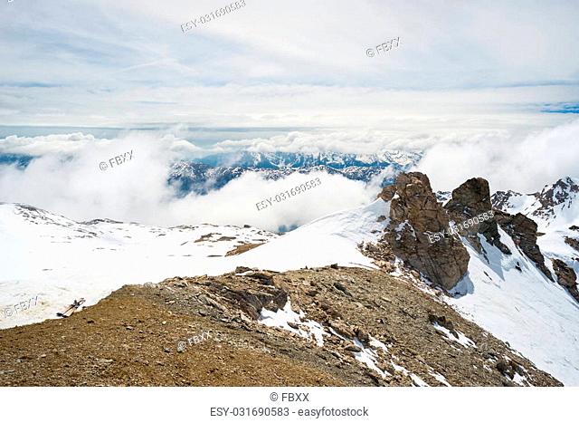 Panoramic view of high mountain peaks and snowcapped ridges at high altitude in the italian french alpine arc. Scenic sky and clouds covering the valley below