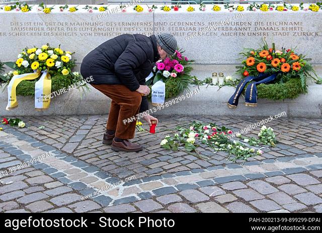 13 February 2020, Saxony, Dresden: A man places a grave light on the Altmarkt at a memorial for the victims of the bombing of Dresden in the Second World War 75...