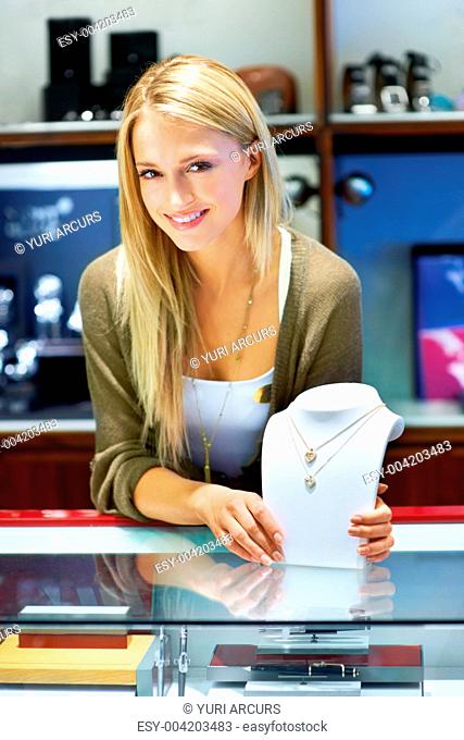 Beautiful blonde jewellery store clerk showing two necklaces on a bust display to the camera
