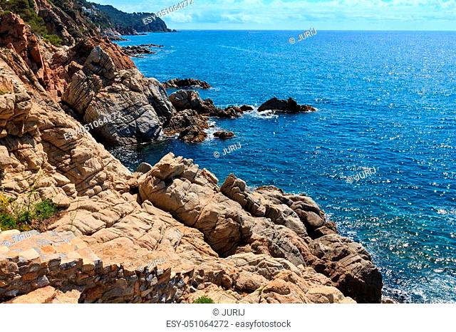 Summer sea rocky coast view with sunny sparkles on water surface and stony stairs (Costa Brava, Spain)