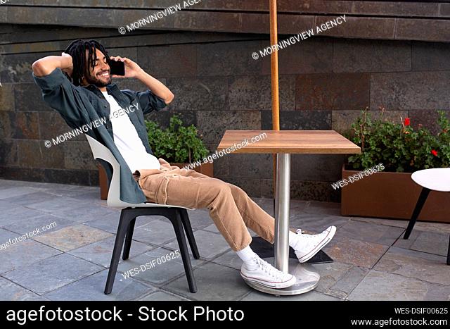 Happy man talking over smart phone sitting on chair at cafe