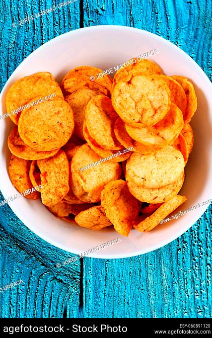 Spicy potato chips in white bowl on blue wooden board
