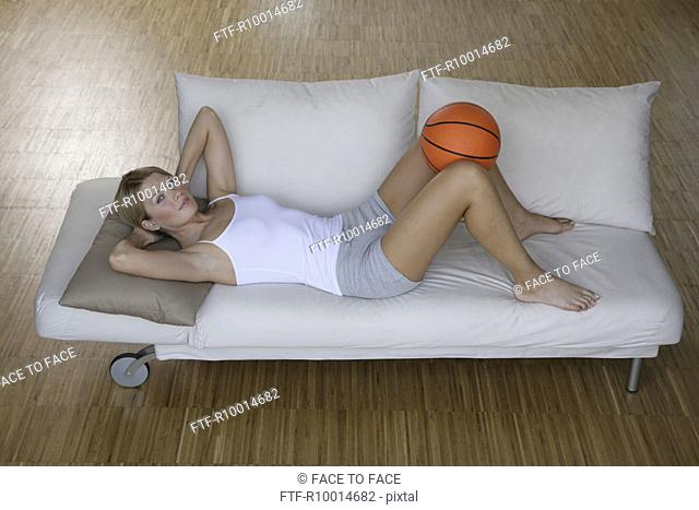 A blonde woman exercising as she holds a basket ball between her legs