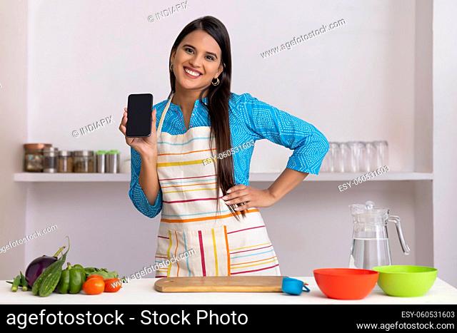 Indian lady posing with smartphone in kitchen