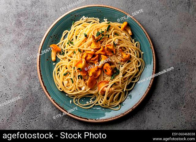 Pasta spaghetti with wild forest mushrooms chanterelles on plate. Seasonal autumn dish on rustic concrete background from above
