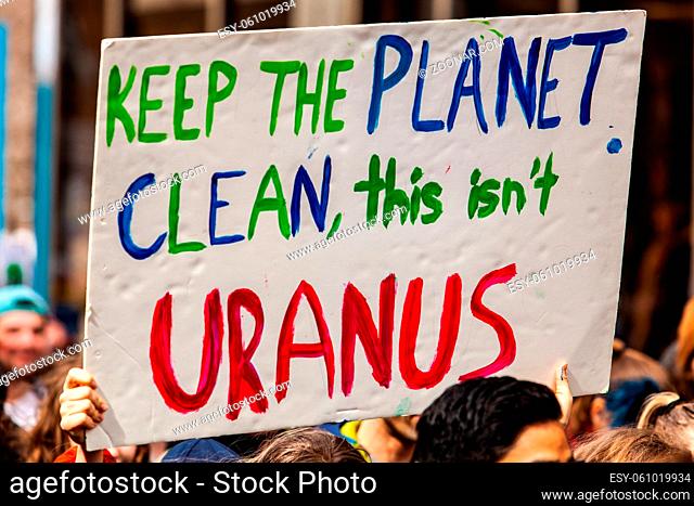 A colorful poster is viewed up close, saying keep the planet clean, this isn't uranus, held by environmentalists as they march in a city center