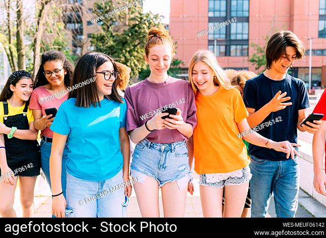 Happy friends using mobile phone walking together on sunny day