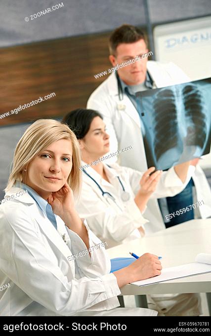 Smiling female medical doctor looking at camera, doctors consulting diagnosis of x-ray image in background