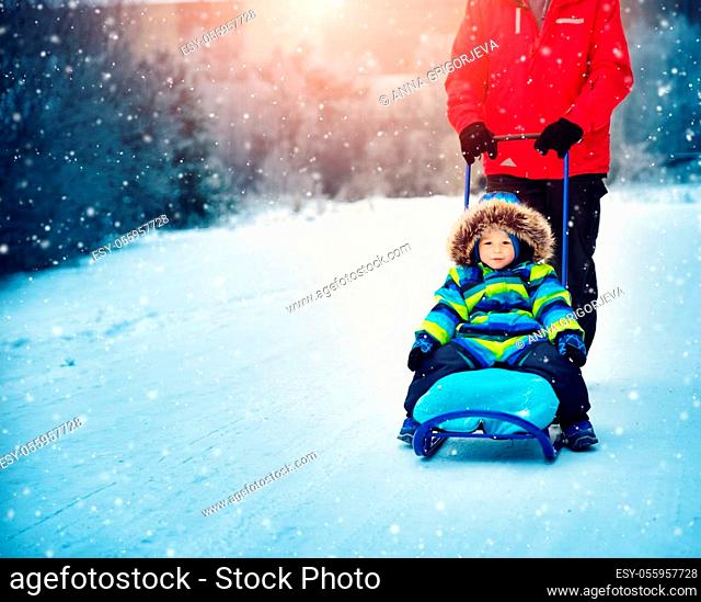 Father with sons walking at snowfall. Children in winter clothes playing with snow and sledding with dad