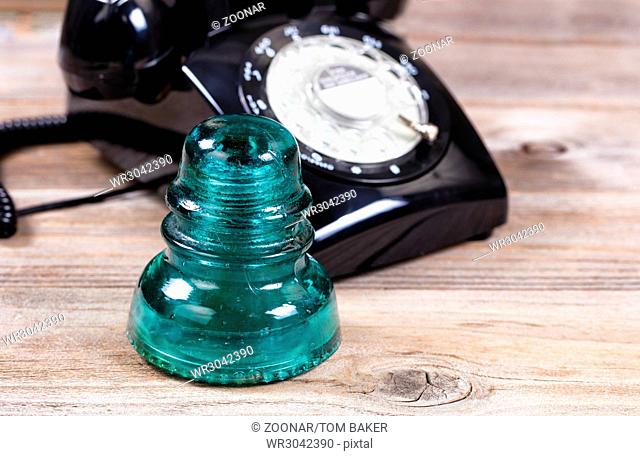 Antique glass insulator and rotary dial phone on rustic wooden boards
