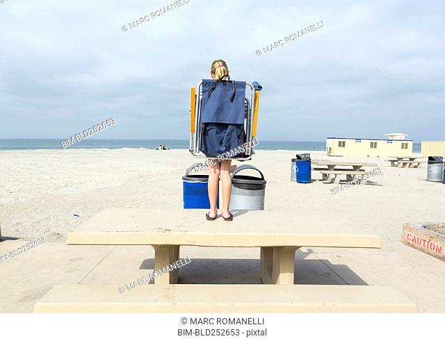 Caucasian girl carrying folding chair on picnic table at beach