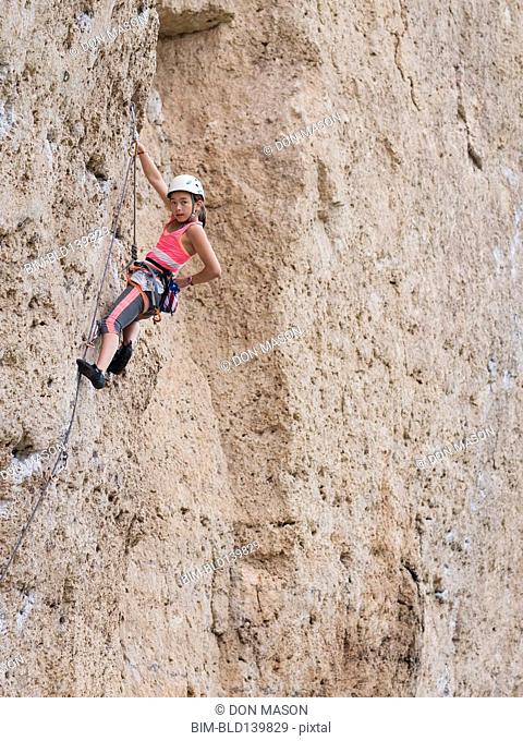 Mixed race girl climbing steep cliff