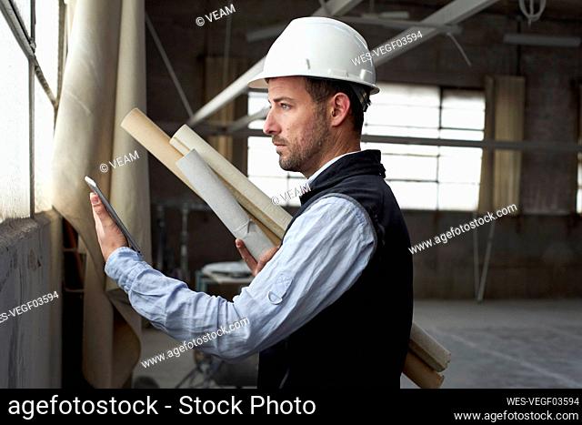 Male real estate developer holding blueprint using digital tablet while standing in building
