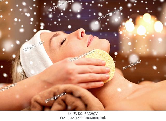 people, beauty, spa, cosmetology and relaxation concept - close up of beautiful young woman lying with closed eyes having face cleaning by sponge and beautician...