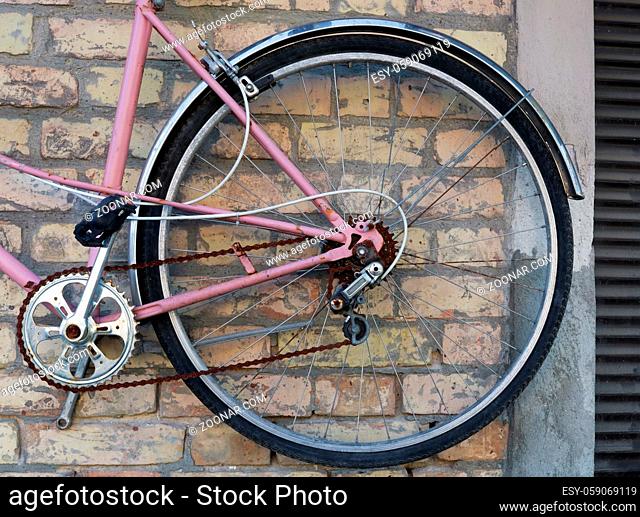 Wheel of broken pink retro bike hanging on a yellow brick wall