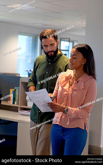Biracial business colleagues discussing over document while walking together at modern workplace