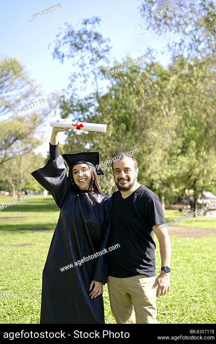 Young girl recently graduated, dressed in cap and gown, with her degree in her hand, celebrating with her family on the university campus
