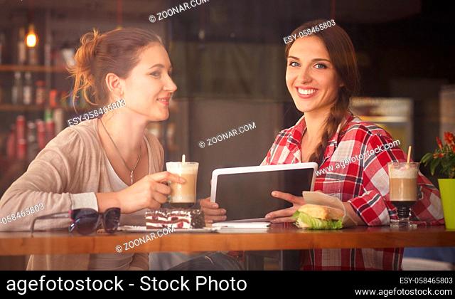 Toned image of best friends communivating or talking while sitting in restaurant or cafe. Ladies looking at tablet PC