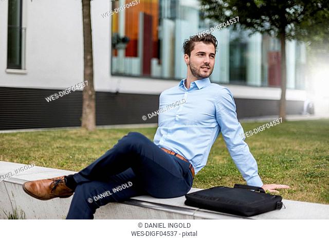 Smiling businessman sitting outdoors looking sideways
