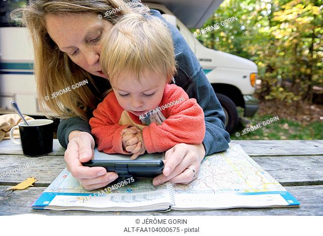 Mother holding child on lap while using atlas and GPS to plan road trip