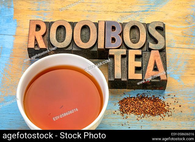 rooibos red tea - a white cup of a hot drink, loose leaves and typography in letterpress wood type on grunge wood background