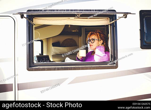 Outside view of pretty traveler lady having leisure relax inside her camper van viewed from the window. Vehicle reanting holiday vacation and van life lifestyle...
