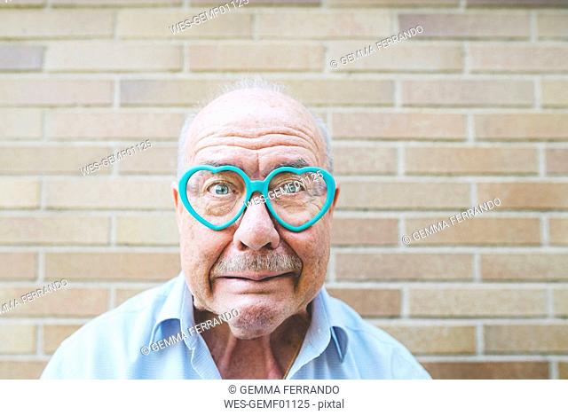 Portrait of senior man wearing heart-shaped glasses pulling funny faces