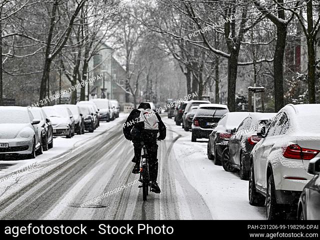 06 December 2023, Berlin: A cyclist rides on a snow-covered road in Karlshorst on which the tracks of cars can be seen. There is a risk of black ice due to...