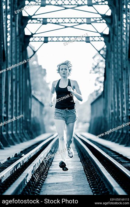 Athlete running on railaway bridge training for marathon and fitness. Healthy sporty caucasian woman exercising in urban environment before going to work