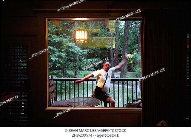 An older asian man performing silly martial arts moves in front of a window with a forest behind him in Yosemite National Park