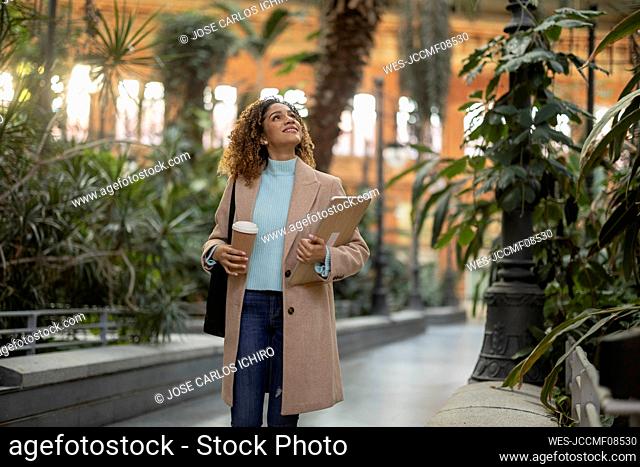 Smiling businesswoman holding laptop and disposable cup
