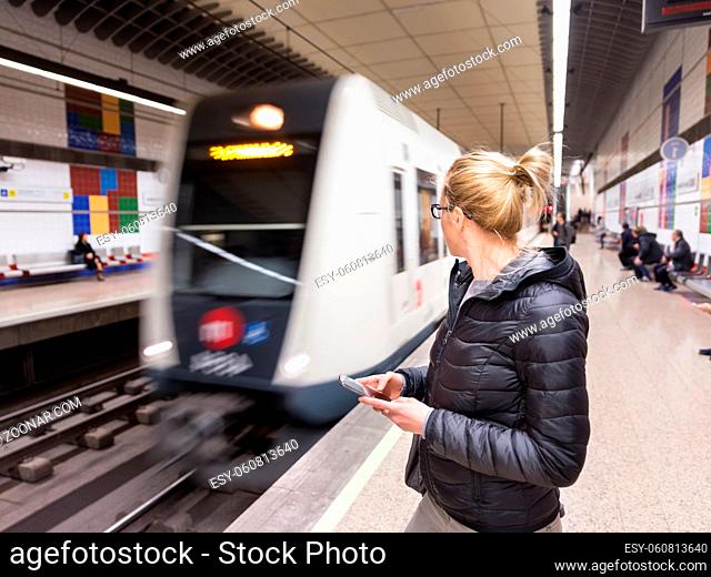 Young casual woman with a cell phone in her hand waiting on the platform of a metro station for metro to arrive. Public transport