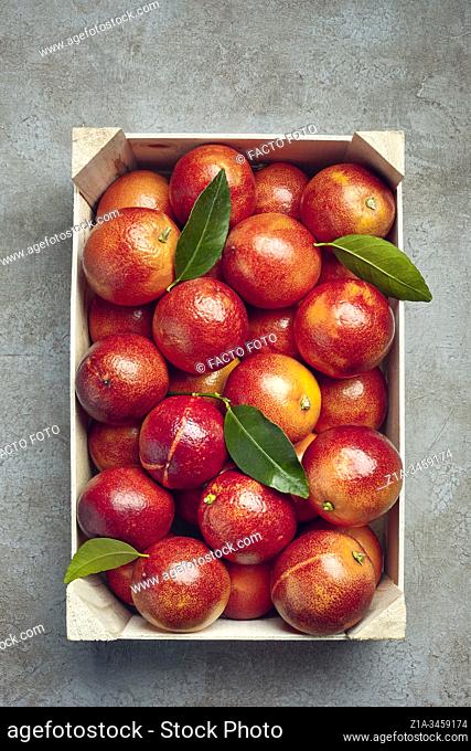 Blood oranges and orange tree leaves in a wooden box on a grey textured background