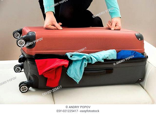 Close-up Of Woman Trying To Close Suitcase With Excess Of Clothes
