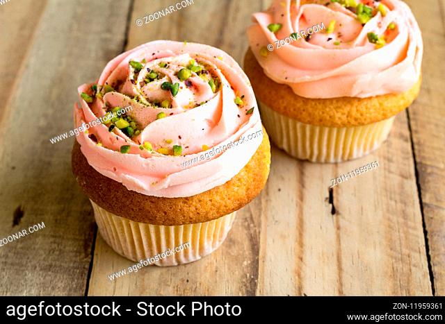 Two pink cup cakes on rustic wooden table close up