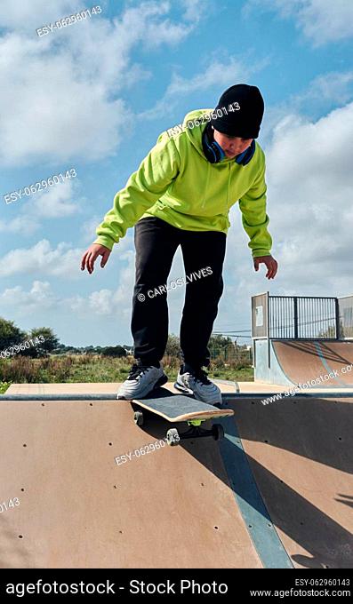 young, teenager, with a skateboard, diving down the slope, on a rink, skateboarding, wearing headphones, green sweatshirt, black hat, swinging, on a sunny day
