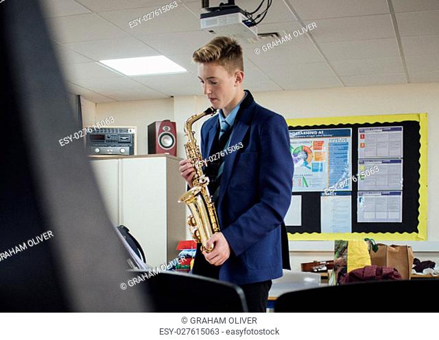 Male student is practicing saxaphone after school in the music room